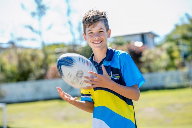 Student in school uniform smiling while holding a rugby ball outdoors