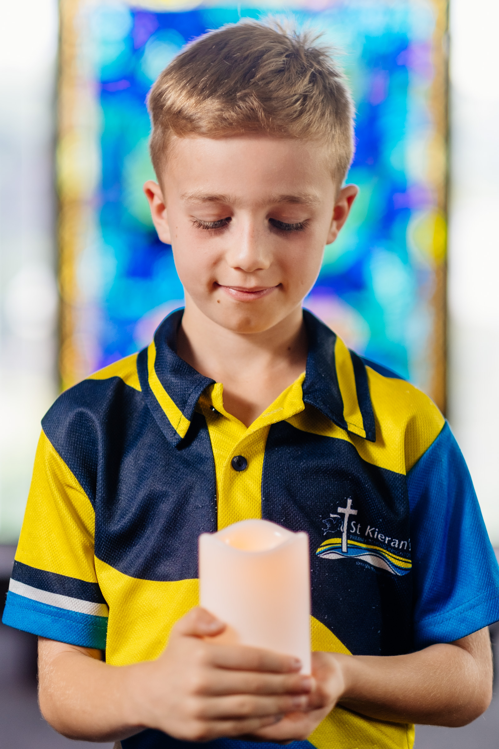 Student in school uniform holding a lit candle with stained glass in the background