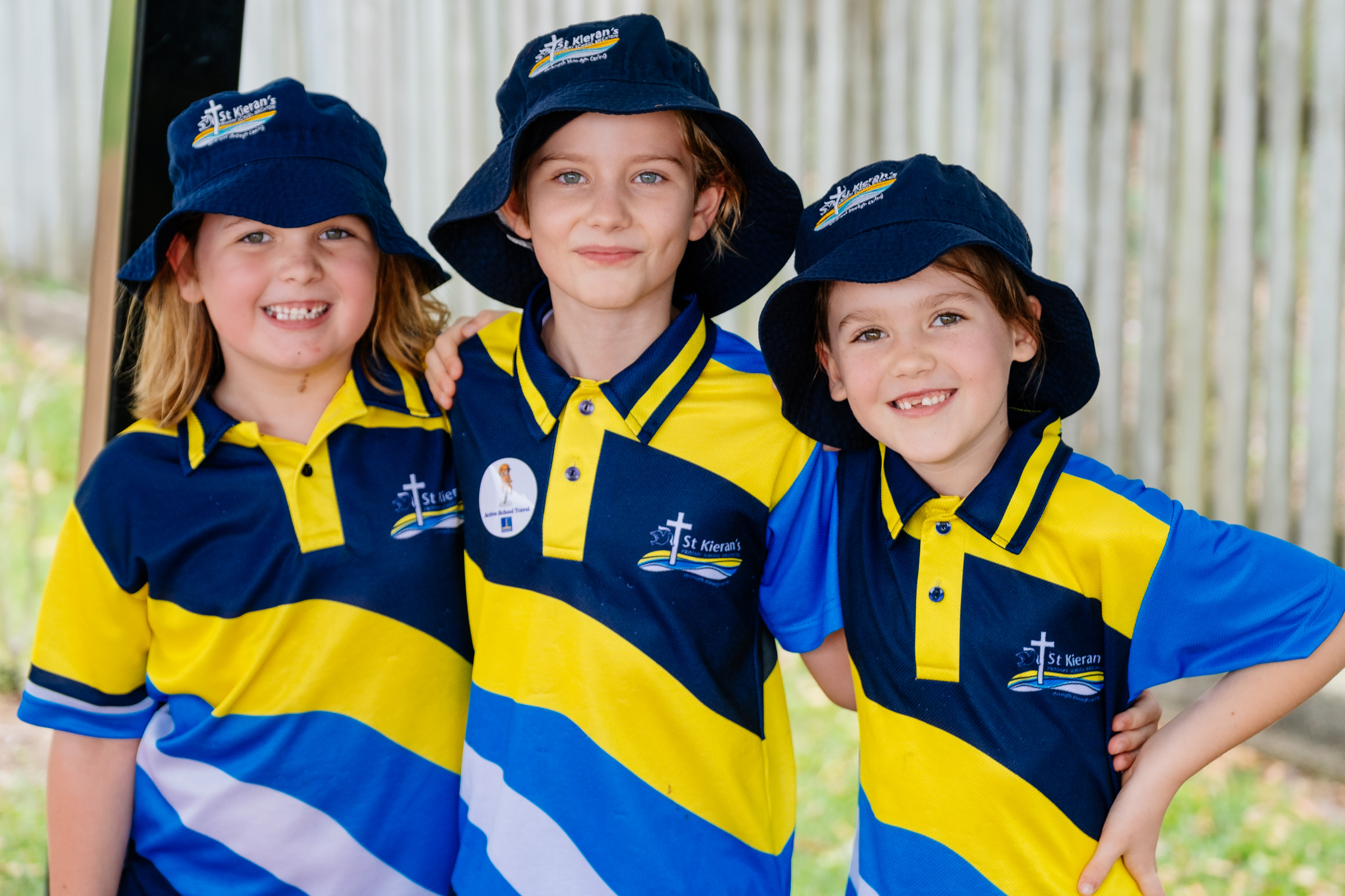 Three students in school uniforms smiling with their arms around each other outdoors