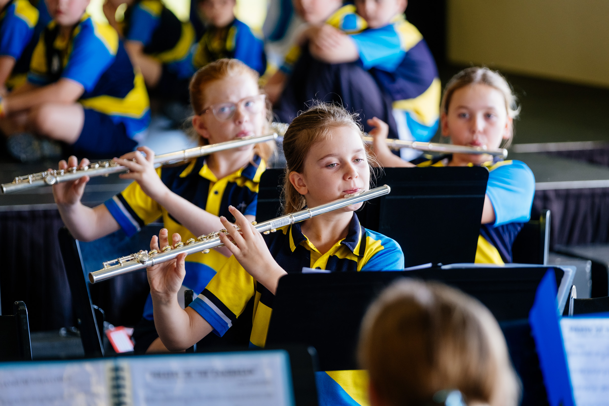 Students in school uniforms playing flutes as part of a seated school band ensemble