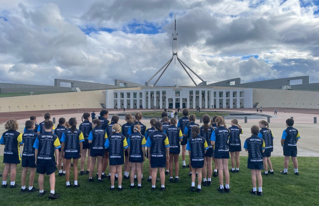 Group of students in school uniforms standing on grass facing Parliament House in Canberra
