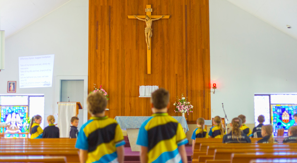 Students in school uniforms standing inside a church facing the altar and crucifix