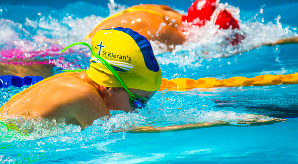 Student wearing a swim cap and goggles swimming in a pool during a race